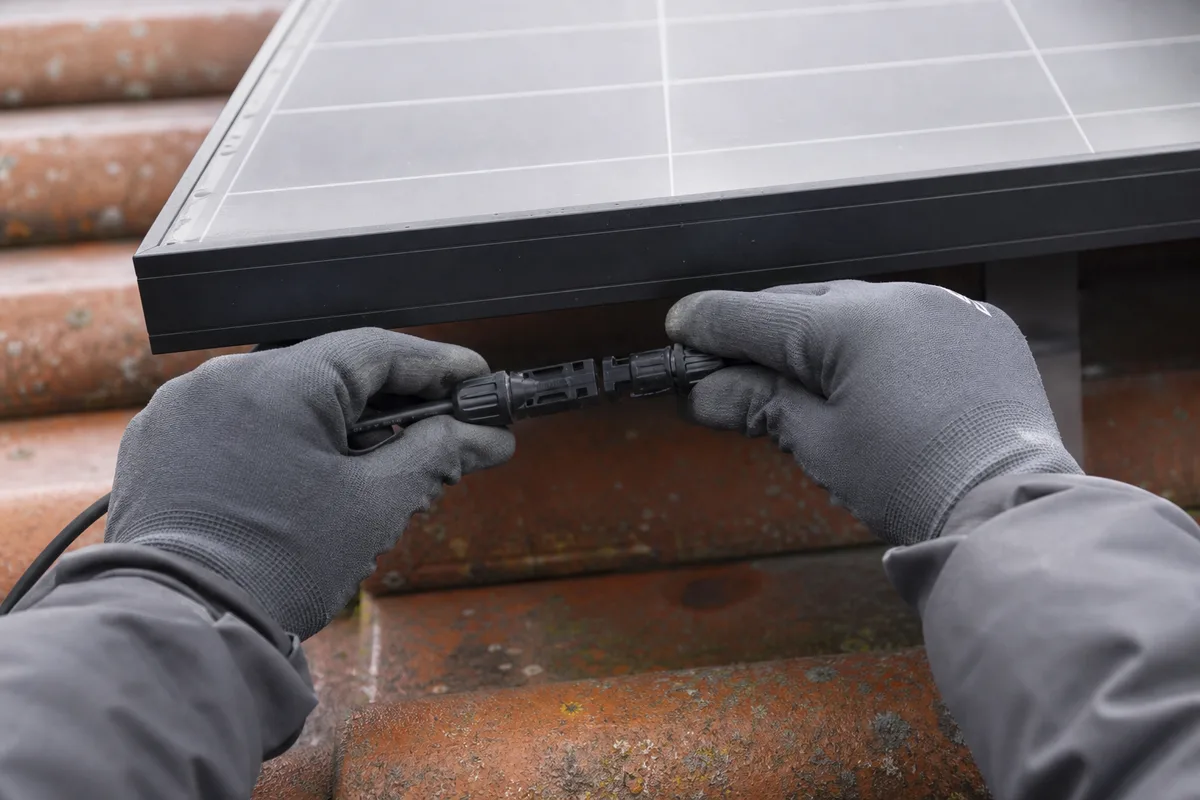 Mains gantées d un technicien raccordant un connecteur de câble solaire sous un module photovoltaïque